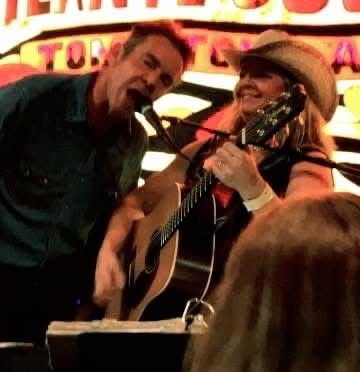 Greg and Kiri sharing a microphone and guitar on stage