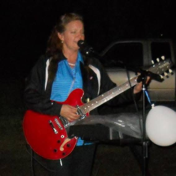 Kiri Hall singing and playing red electric guitar at an outdoor show