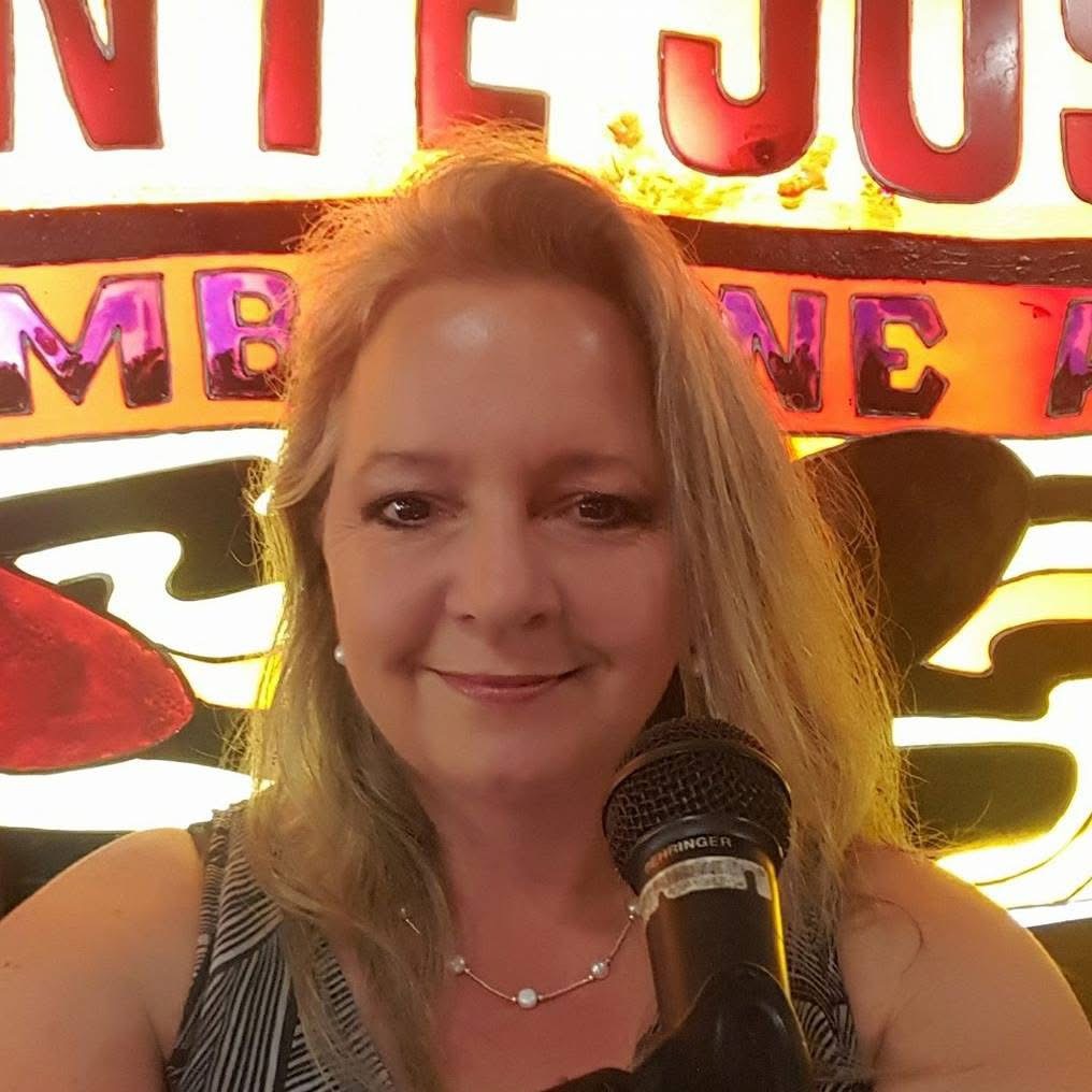 Kiri Hall smiling at a microphone in front of a neon sign